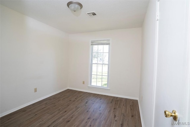 unfurnished room featuring dark wood finished floors, visible vents, and baseboards