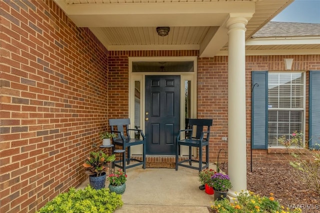 view of exterior entry with a shingled roof and brick siding