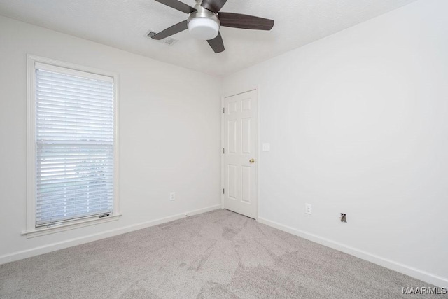 empty room featuring light colored carpet, visible vents, ceiling fan, and baseboards