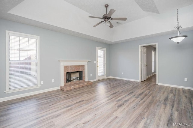 unfurnished living room featuring a tray ceiling, a tile fireplace, wood finished floors, and baseboards