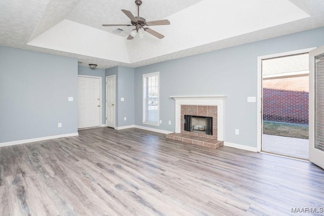 unfurnished living room featuring light wood finished floors, a tray ceiling, a tiled fireplace, and baseboards