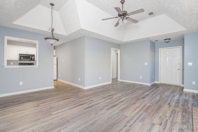 unfurnished living room featuring light wood-type flooring, baseboards, a tray ceiling, and a textured ceiling