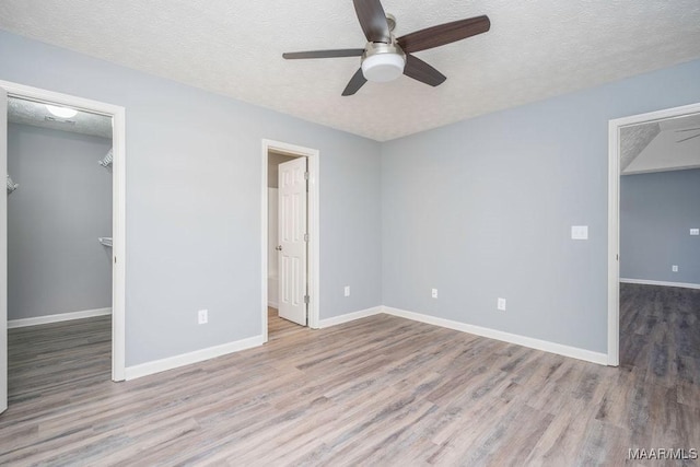 unfurnished bedroom featuring a textured ceiling, a spacious closet, light wood finished floors, and baseboards