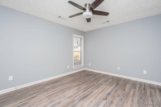 empty room featuring baseboards, a textured ceiling, visible vents, and wood finished floors