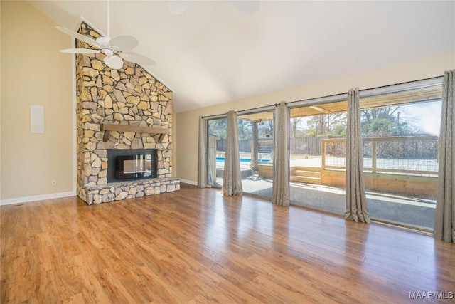 unfurnished living room with ceiling fan, a stone fireplace, wood finished floors, high vaulted ceiling, and baseboards