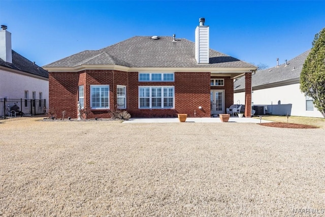 rear view of property featuring a shingled roof, a chimney, fence, a patio area, and brick siding