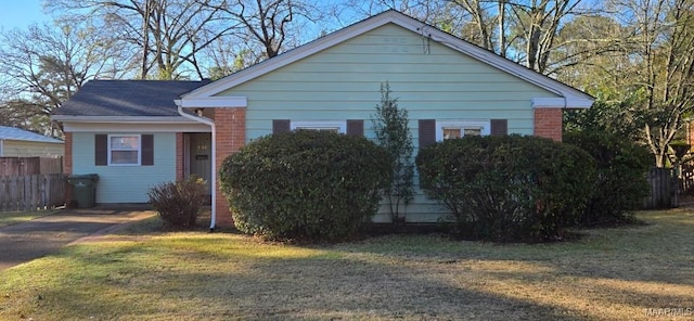 view of side of property with brick siding, a lawn, and fence