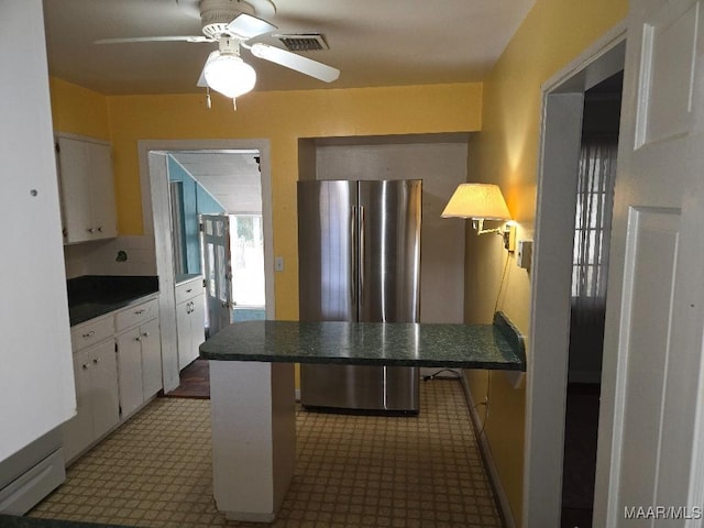 kitchen with a peninsula, visible vents, white cabinetry, freestanding refrigerator, and dark countertops