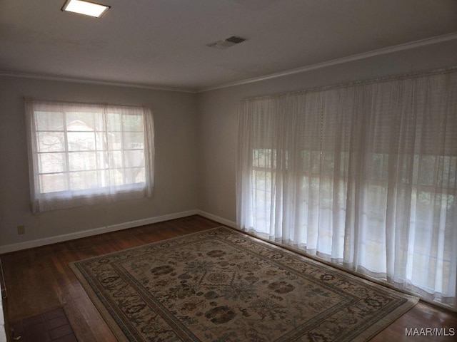 unfurnished room featuring dark wood-style floors, visible vents, crown molding, and baseboards