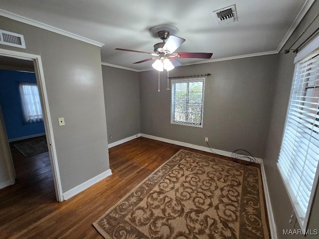 empty room with baseboards, visible vents, dark wood-type flooring, and crown molding