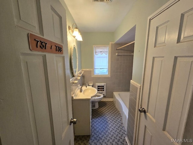 bathroom featuring toilet, tile patterned floors, heating unit, vanity, and tile walls