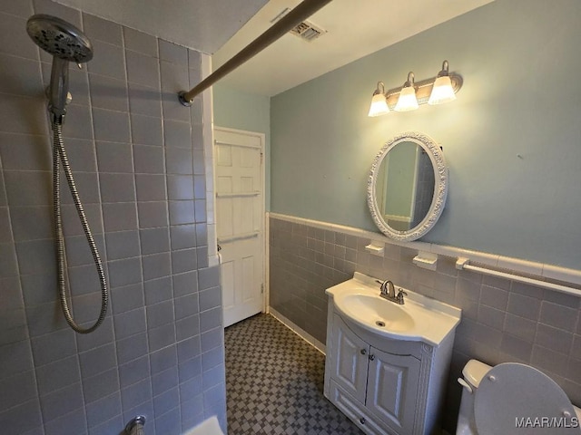 bathroom with tile walls, visible vents, toilet, wainscoting, and vanity