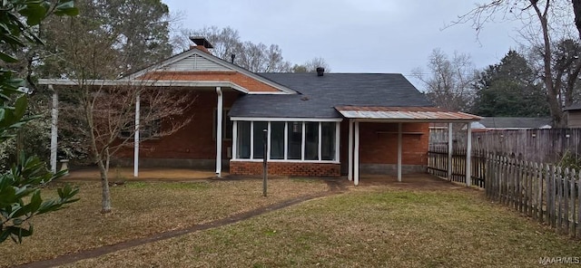 rear view of property featuring brick siding, a lawn, fence, and a sunroom