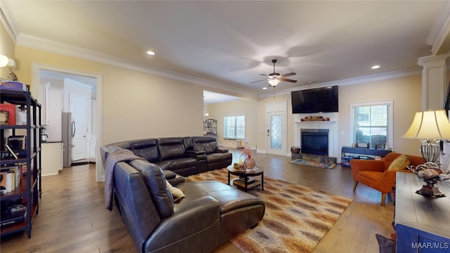 living area with a fireplace with raised hearth, ornamental molding, and wood finished floors