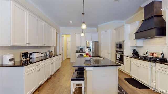 kitchen with white cabinets, an island with sink, hanging light fixtures, custom exhaust hood, and stainless steel appliances