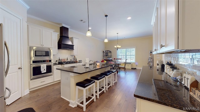 kitchen featuring stainless steel appliances, white cabinetry, custom range hood, an island with sink, and pendant lighting