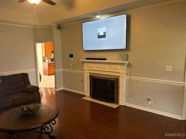 living room with a tiled fireplace, ornamental molding, ceiling fan, wood finished floors, and baseboards