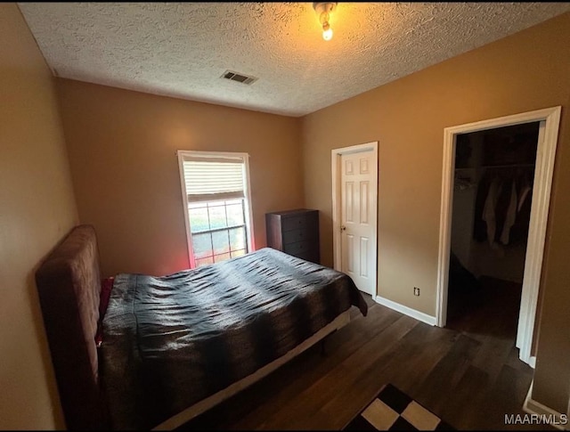 bedroom with a walk in closet, dark wood-style flooring, visible vents, a textured ceiling, and baseboards