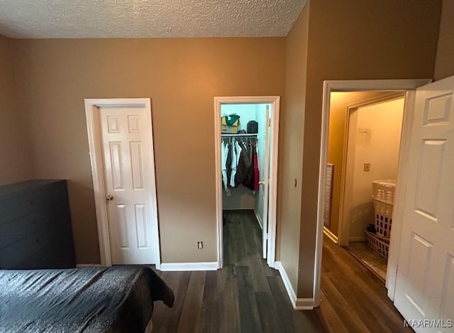 bedroom with a closet, a spacious closet, dark wood-type flooring, a textured ceiling, and baseboards