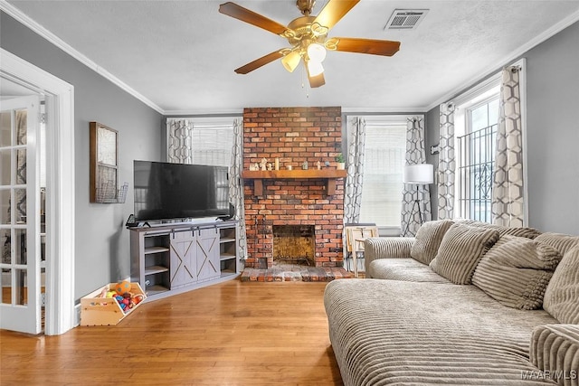 living area featuring visible vents, a ceiling fan, ornamental molding, wood finished floors, and a fireplace