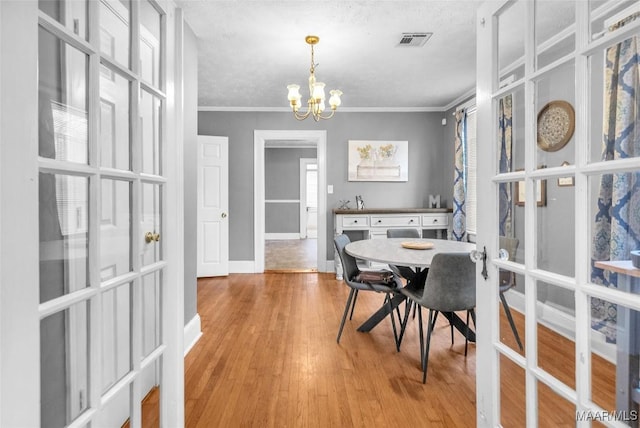 dining room featuring baseboards, visible vents, ornamental molding, an inviting chandelier, and light wood-style floors