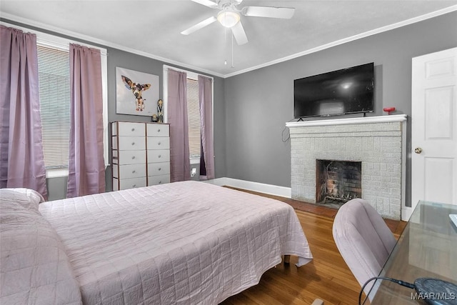 bedroom featuring baseboards, ceiling fan, wood finished floors, crown molding, and a fireplace