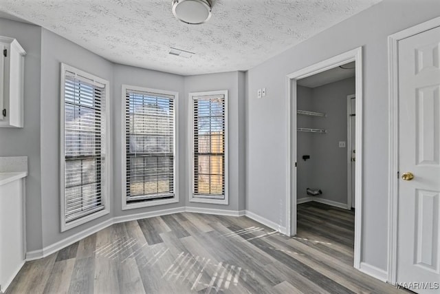 unfurnished dining area with a textured ceiling, baseboards, and wood finished floors