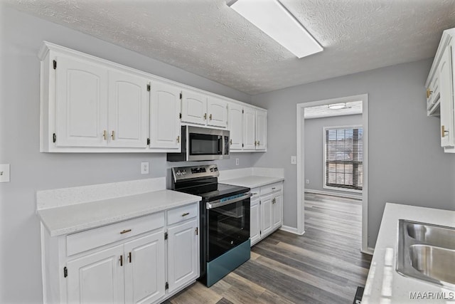 kitchen with dark wood-style flooring, stainless steel appliances, light countertops, white cabinetry, and a sink