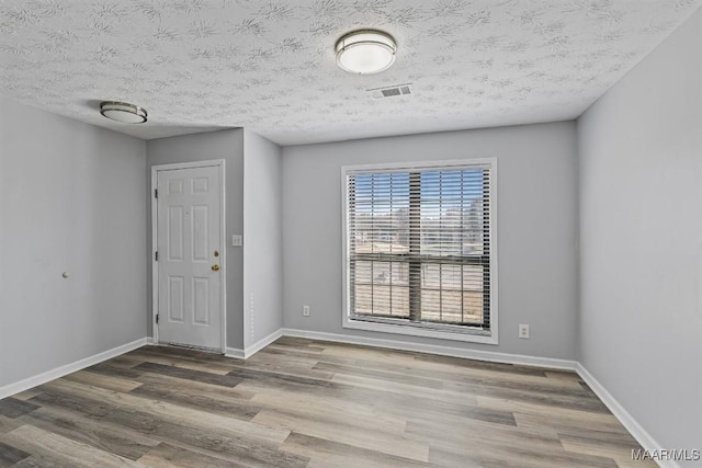 unfurnished room featuring visible vents, a textured ceiling, baseboards, and wood finished floors