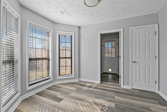 spare room with a textured ceiling, baseboards, and wood finished floors