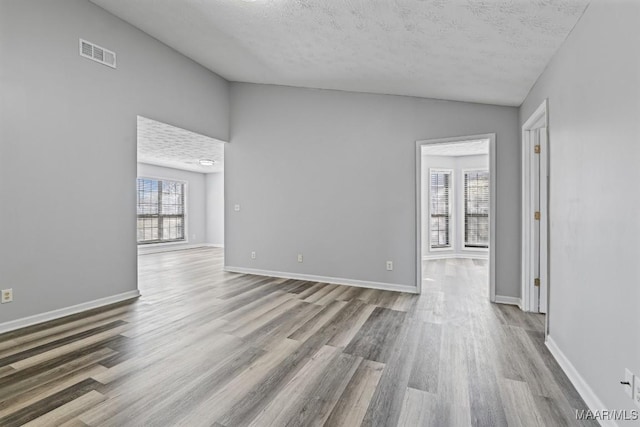 empty room with visible vents, vaulted ceiling, baseboards, and wood finished floors