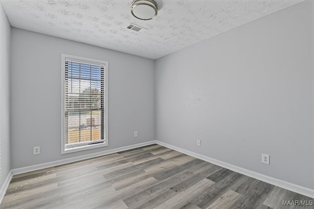 spare room featuring a textured ceiling, wood finished floors, visible vents, and baseboards