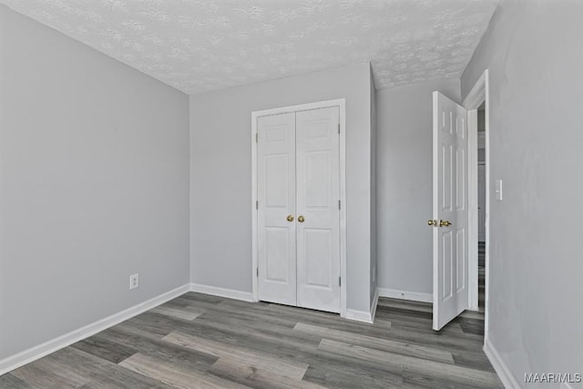 unfurnished bedroom with a textured ceiling, baseboards, and wood finished floors