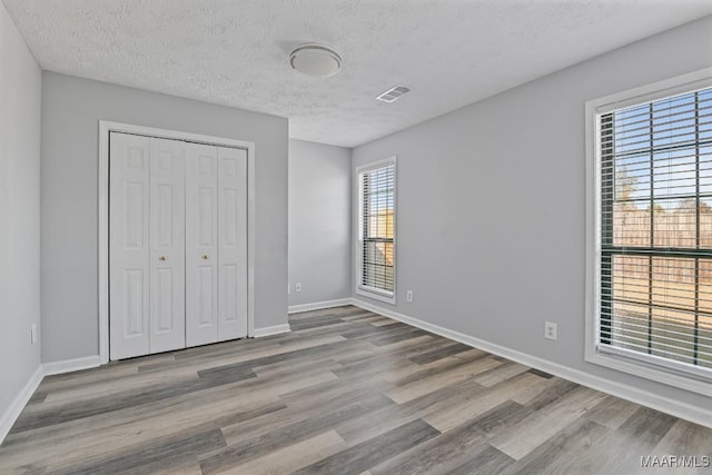 unfurnished bedroom featuring baseboards, a textured ceiling, visible vents, and wood finished floors