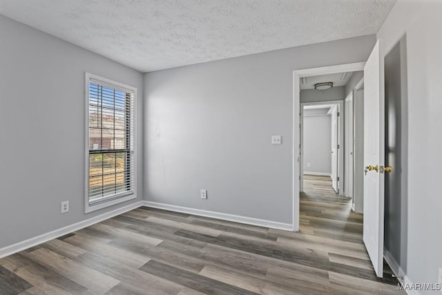 unfurnished room featuring attic access, a textured ceiling, baseboards, and wood finished floors