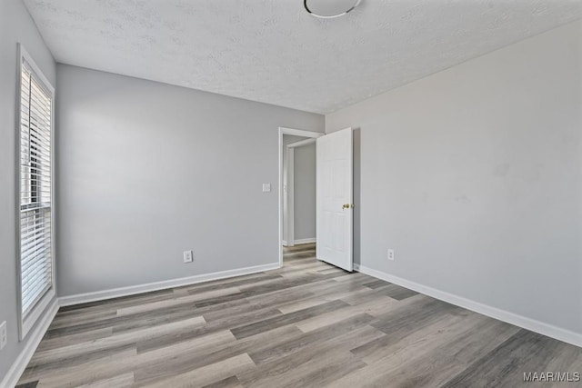 spare room featuring a textured ceiling, baseboards, and wood finished floors