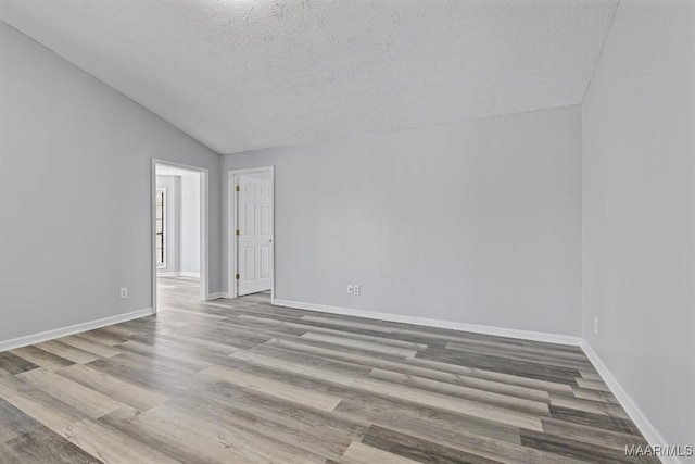 spare room featuring vaulted ceiling, a textured ceiling, wood finished floors, and baseboards