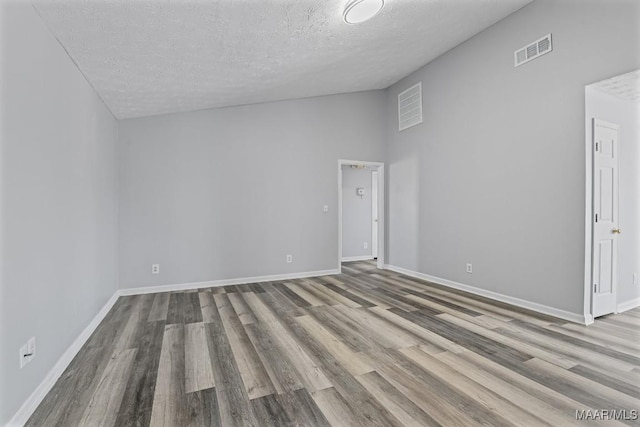 empty room with lofted ceiling, visible vents, baseboards, and wood finished floors