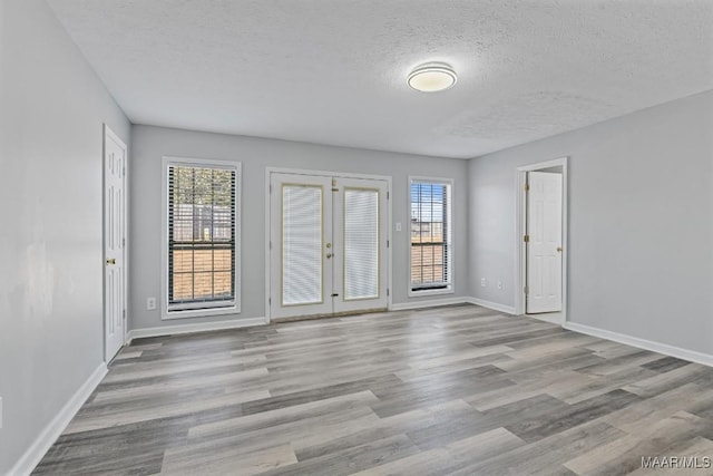 unfurnished room with a textured ceiling, french doors, wood finished floors, and a wealth of natural light