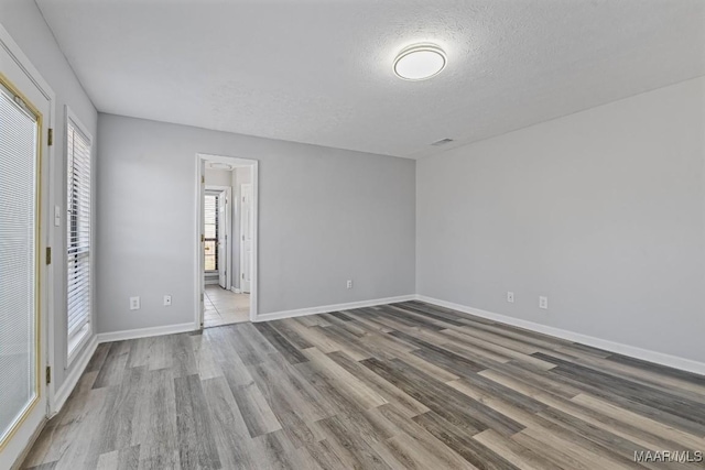 spare room with a textured ceiling, wood finished floors, and baseboards