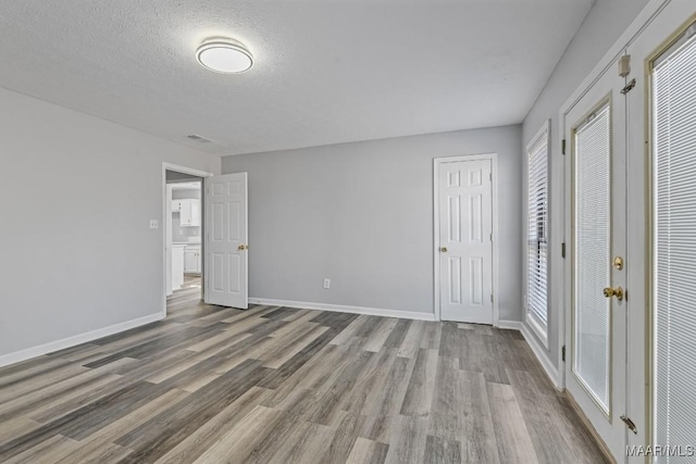 unfurnished bedroom featuring two closets, a textured ceiling, baseboards, and wood finished floors