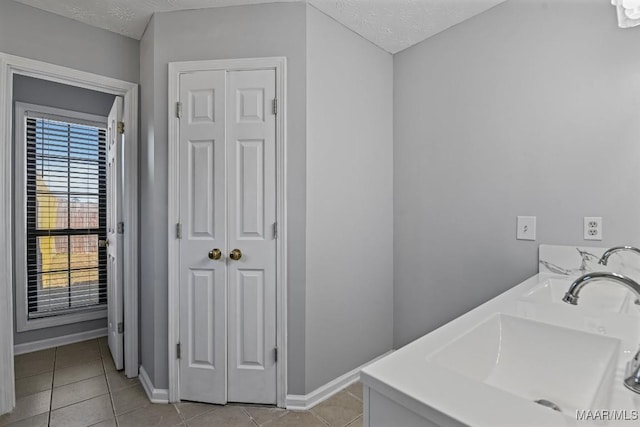 bathroom with a textured ceiling, tile patterned flooring, a sink, baseboards, and a closet