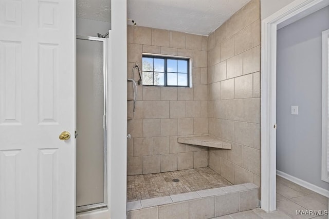 full bath featuring tile patterned flooring, baseboards, a shower stall, and a textured ceiling