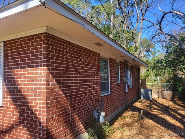 view of side of property with brick siding, fence, and central air condition unit