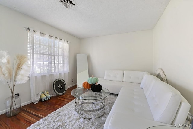 living area featuring a textured ceiling, wood finished floors, visible vents, and baseboards