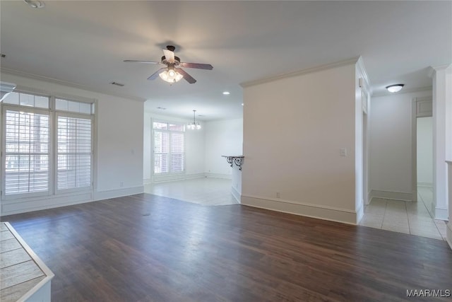 unfurnished living room featuring dark wood-style floors, visible vents, ornamental molding, and ceiling fan with notable chandelier