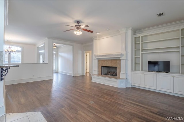 unfurnished living room with dark wood-style flooring, visible vents, ornamental molding, a tile fireplace, and ceiling fan with notable chandelier