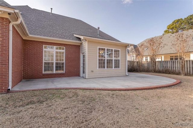 back of house featuring a lawn, a patio, roof with shingles, fence, and brick siding