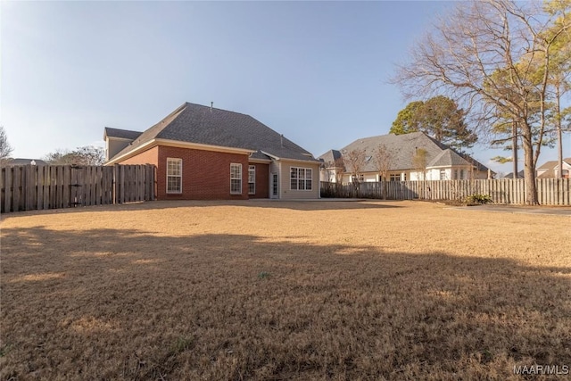 rear view of property with a fenced backyard, a lawn, and brick siding