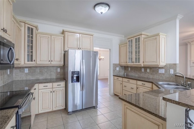 kitchen with glass insert cabinets, appliances with stainless steel finishes, dark stone countertops, crown molding, and a sink